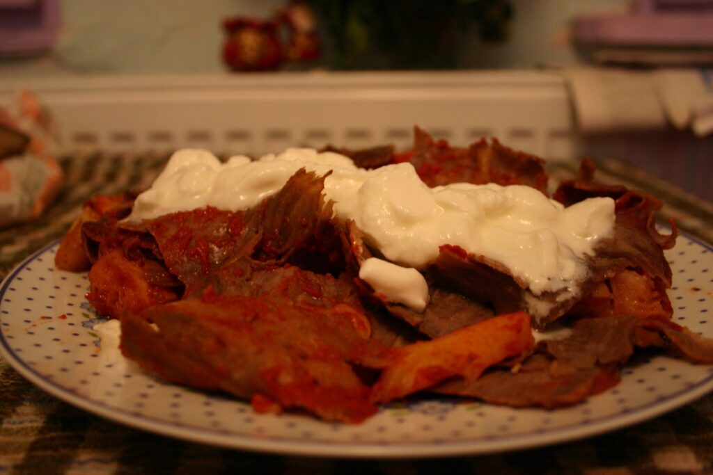 İskender kebab — mishi i prerë hollë mbi bukë pide me salcë domatesh  kos dhe gjalpë të shkrirë