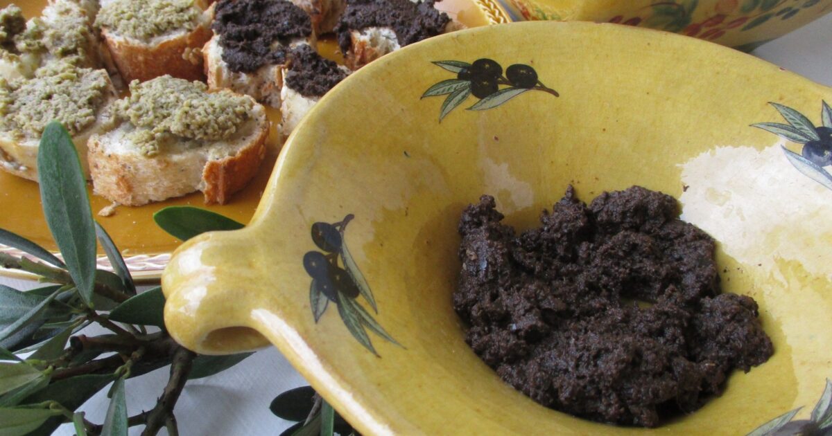 Tapenade me ullinj të zi në tas dhe mbi bukë të thekur