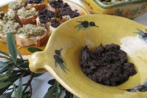 Tapenade me ullinj të zi në tas dhe mbi bukë të thekur