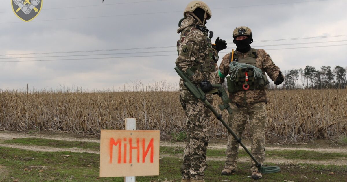 Ushtarë ukrainas të deminimit në një fushë me tabelë paralajmëruese për mina