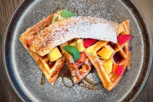 Waffle belge me luleshtrydhe dhe fruta të freskëta, shurup panje dhe sheqer pluhur